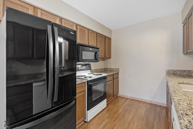 kitchen with black appliances, sink, light hardwood / wood-style floors, light stone counters, and a textured ceiling