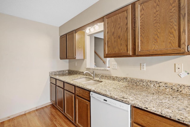 kitchen with white dishwasher, sink, light hardwood / wood-style floors, and light stone countertops