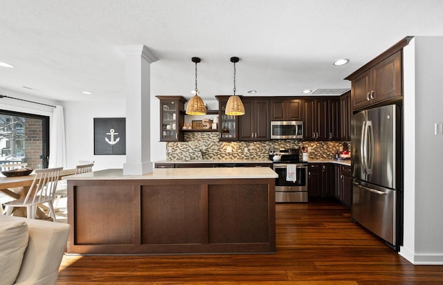 kitchen with stainless steel appliances, hanging light fixtures, dark brown cabinets, and decorative columns