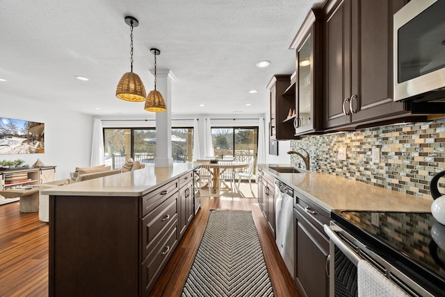 kitchen with dark brown cabinetry, sink, hanging light fixtures, appliances with stainless steel finishes, and a kitchen island