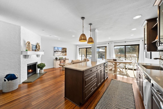 kitchen featuring a kitchen island, dishwasher, a brick fireplace, dark brown cabinets, and a textured ceiling