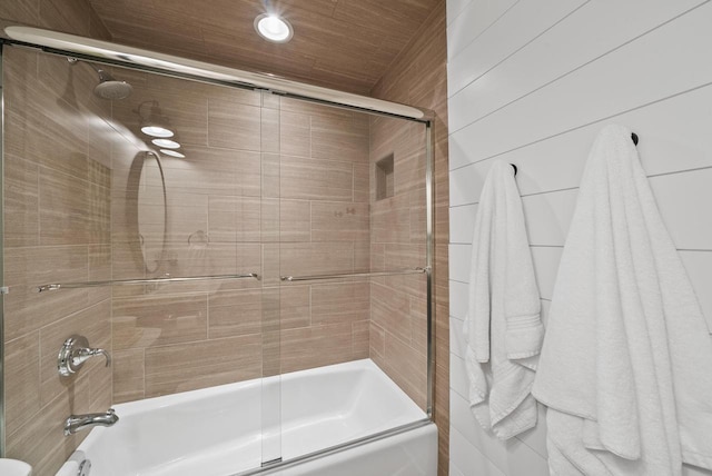 bathroom featuring bath / shower combo with glass door and wood walls