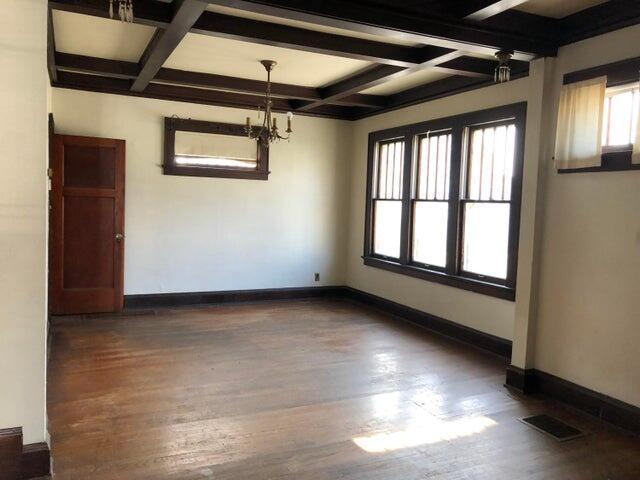 unfurnished dining area featuring an inviting chandelier, coffered ceiling, dark wood-type flooring, and beam ceiling