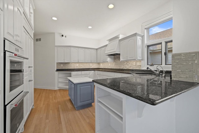 kitchen with blue cabinets, white cabinetry, sink, dark stone counters, and kitchen peninsula