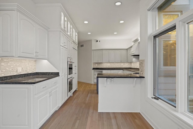 kitchen featuring light hardwood / wood-style flooring, white cabinetry, dark stone countertops, tasteful backsplash, and kitchen peninsula