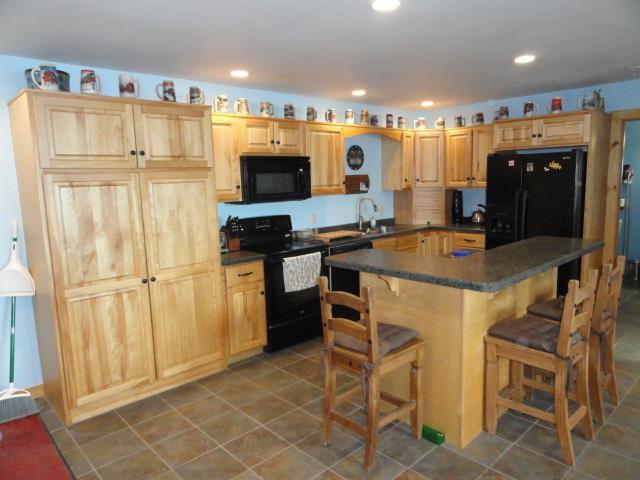 N8621 5th Rd, Westfield, WI 53964 - kitchen with a kitchen bar, light brown cabinetry, sink, a center island, and black appliances