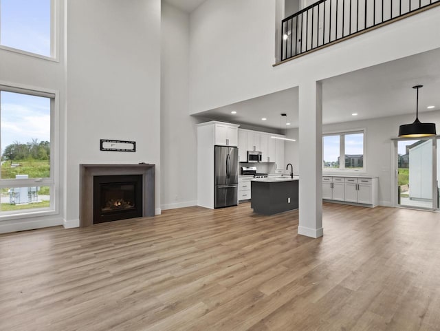 unfurnished living room featuring sink, light hardwood / wood-style floors, and a high ceiling