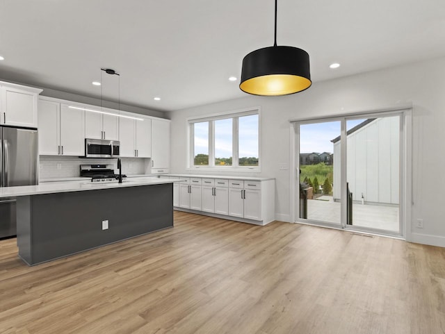 kitchen featuring hanging light fixtures, stainless steel appliances, an island with sink, and white cabinets