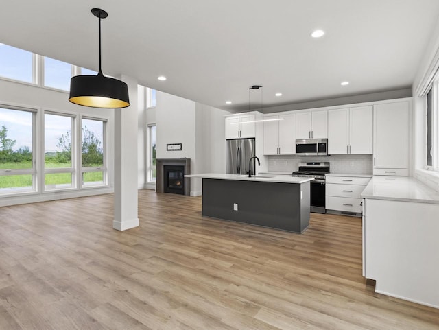 kitchen with sink, appliances with stainless steel finishes, a kitchen island with sink, white cabinets, and decorative light fixtures