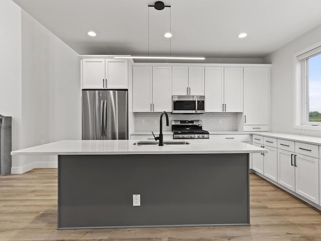 kitchen with appliances with stainless steel finishes, decorative light fixtures, white cabinetry, sink, and a kitchen island with sink