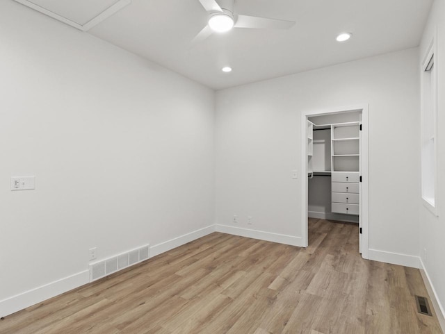 unfurnished bedroom with ceiling fan, a spacious closet, a closet, and light wood-type flooring