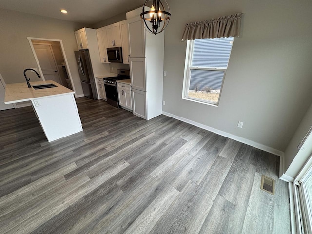 kitchen with sink, hanging light fixtures, appliances with stainless steel finishes, a kitchen island with sink, and white cabinets