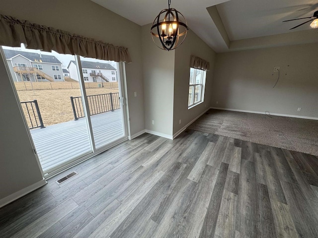 unfurnished dining area with ceiling fan with notable chandelier, a healthy amount of sunlight, and hardwood / wood-style floors