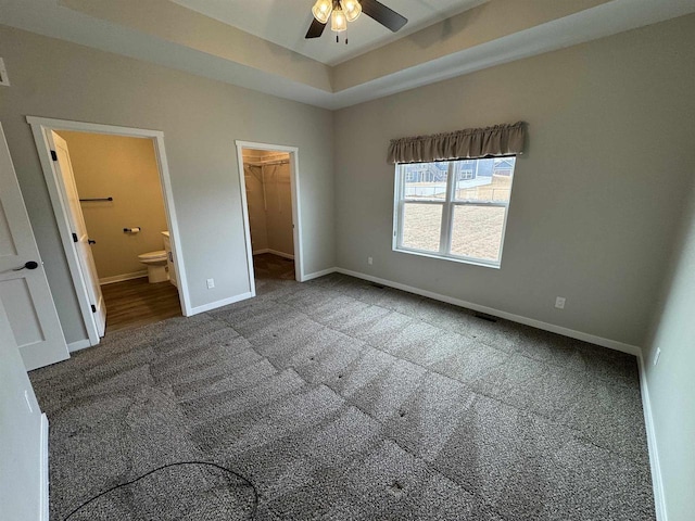 unfurnished bedroom featuring carpet flooring, a spacious closet, ceiling fan, a raised ceiling, and ensuite bath