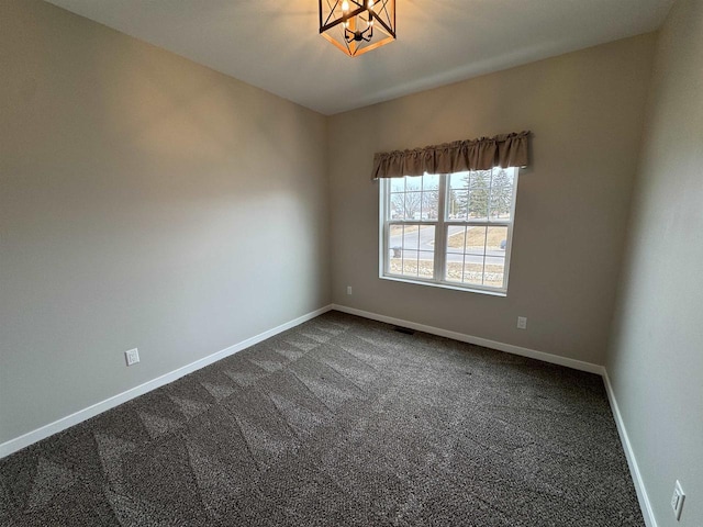 unfurnished room featuring a chandelier and dark carpet