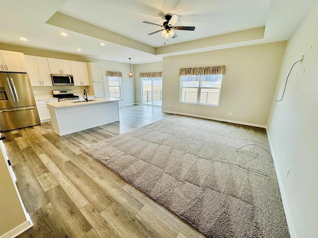 kitchen featuring hanging light fixtures, a tray ceiling, an island with sink, stainless steel appliances, and white cabinets