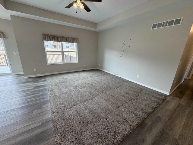 empty room with dark hardwood / wood-style flooring, a raised ceiling, and ceiling fan