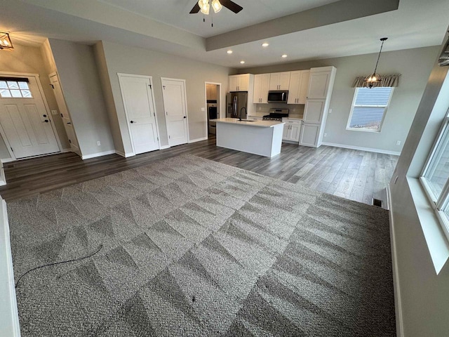 kitchen featuring white cabinetry, wood-type flooring, hanging light fixtures, a kitchen island with sink, and stainless steel appliances