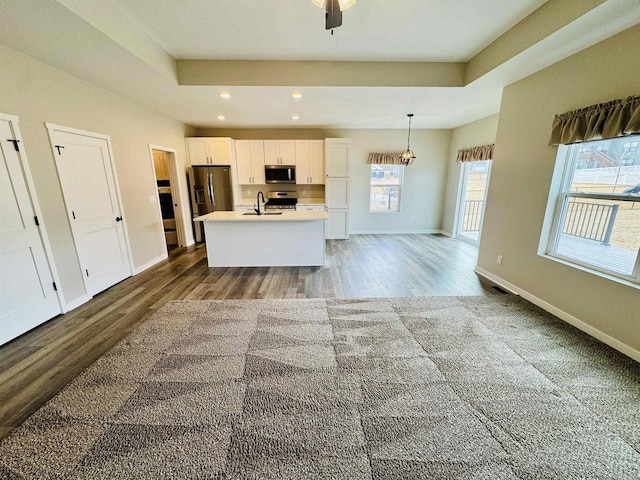 kitchen with a kitchen island with sink, a tray ceiling, white cabinets, and appliances with stainless steel finishes