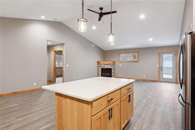 kitchen featuring stainless steel refrigerator, hanging light fixtures, a fireplace, light hardwood / wood-style floors, and a kitchen island