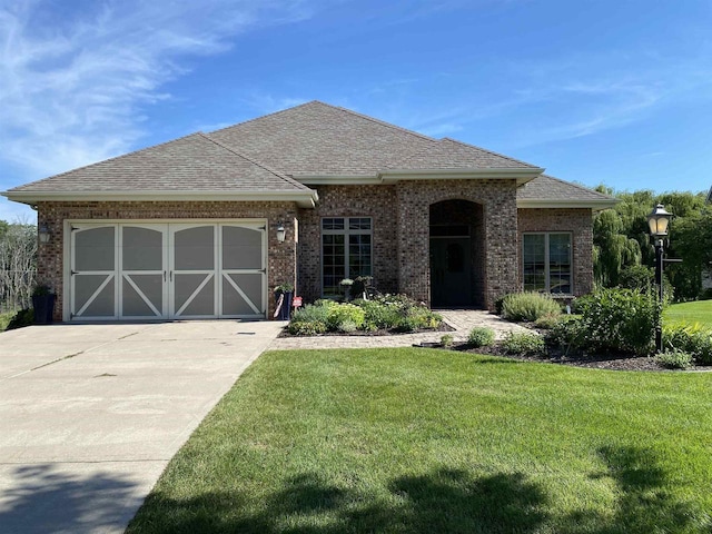 view of front of house with a garage, driveway, brick siding, roof with shingles, and a front yard