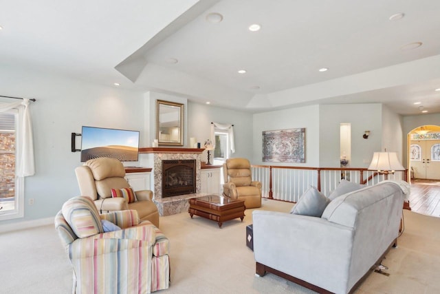 living room with a fireplace with raised hearth, arched walkways, a raised ceiling, and recessed lighting