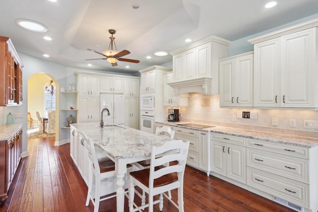 kitchen featuring white appliances, white cabinetry, a kitchen bar, and arched walkways