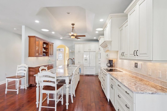 kitchen with arched walkways, white cabinetry, a sink, an island with sink, and white fridge with ice dispenser