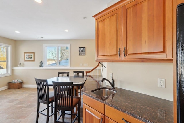 kitchen with dark stone counters, brown cabinets, a sink, and baseboards