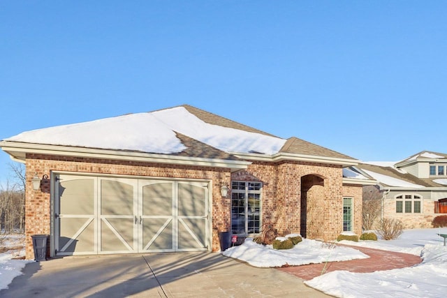 view of front facade featuring a shingled roof, brick siding, driveway, and an attached garage