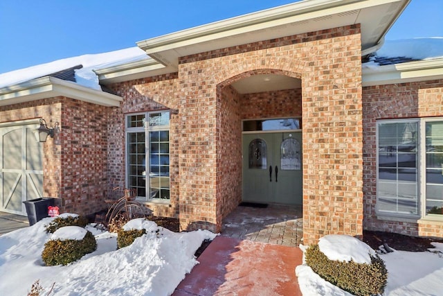 snow covered property entrance featuring a patio area and brick siding