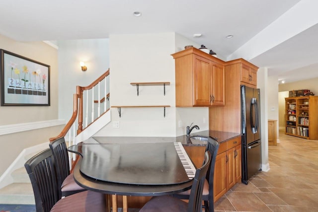 kitchen featuring brown cabinetry, dark stone counters, freestanding refrigerator, a sink, and recessed lighting