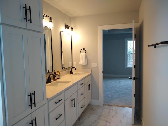 full bath featuring marble finish floor, double vanity, a sink, and baseboards