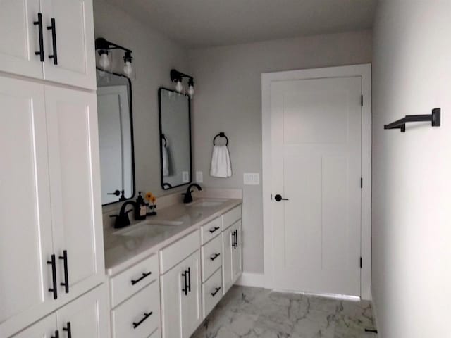 bathroom featuring marble finish floor, double vanity, a sink, and baseboards