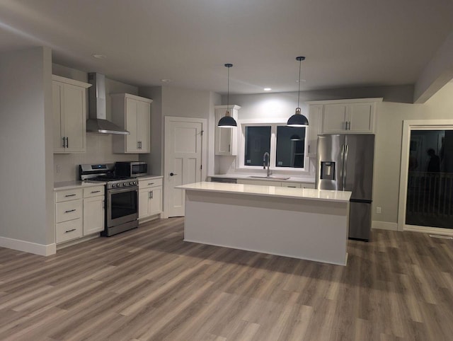 kitchen with a sink, light countertops, appliances with stainless steel finishes, and wall chimney range hood