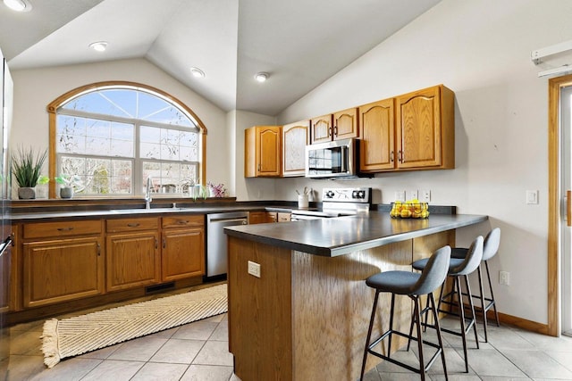 kitchen featuring a sink, dark countertops, stainless steel appliances, a peninsula, and lofted ceiling