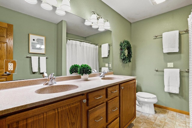 bathroom featuring double vanity, toilet, baseboards, and a sink