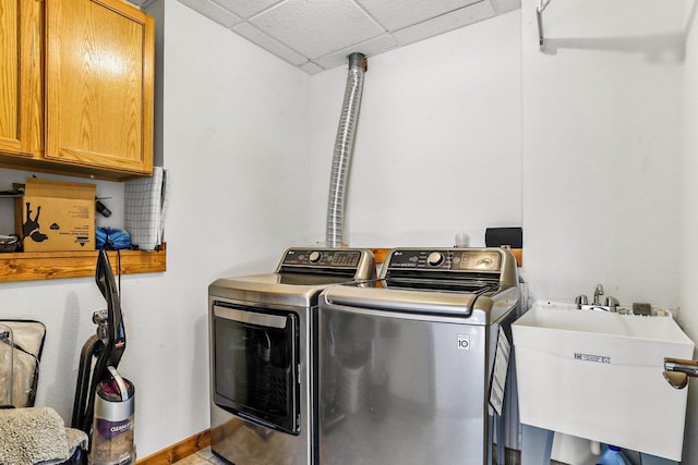 clothes washing area featuring a sink, baseboards, cabinet space, and washer and clothes dryer