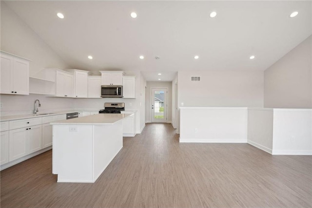 kitchen with stainless steel appliances, a kitchen island, sink, and white cabinets