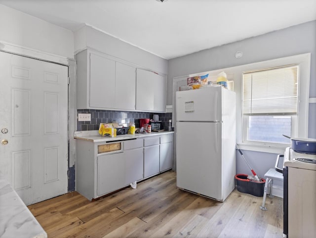 kitchen featuring white refrigerator, white cabinets, light hardwood / wood-style floors, and decorative backsplash