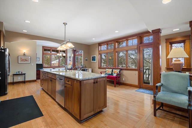 kitchen featuring appliances with stainless steel finishes, pendant lighting, light stone counters, a center island with sink, and light hardwood / wood-style flooring