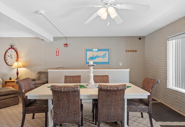 dining room with wooden walls, ceiling fan, and beam ceiling