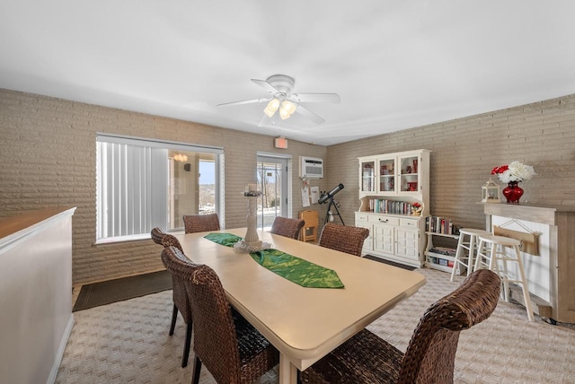 dining room with a fireplace, a wall unit AC, ceiling fan, and brick wall