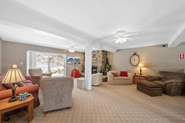 carpeted living room with beamed ceiling, a stone fireplace, and ceiling fan