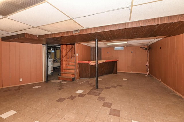 basement featuring water heater, a paneled ceiling, and wooden walls