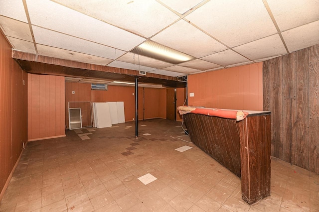 basement with bar, wooden walls, and a drop ceiling