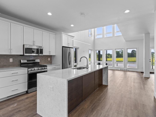 kitchen with sink, white cabinetry, a center island with sink, appliances with stainless steel finishes, and dark hardwood / wood-style floors