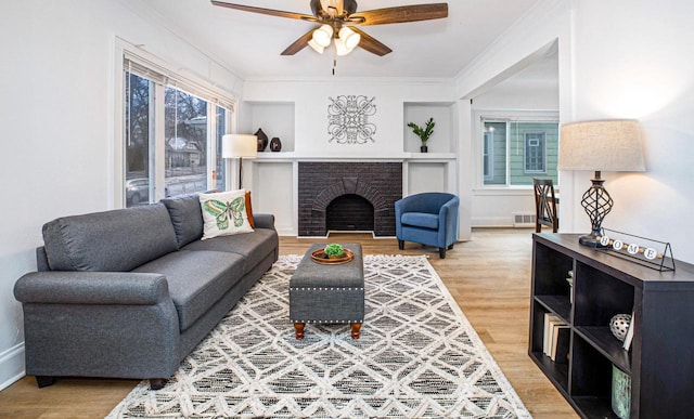 living room featuring crown molding, plenty of natural light, a brick fireplace, and hardwood / wood-style flooring