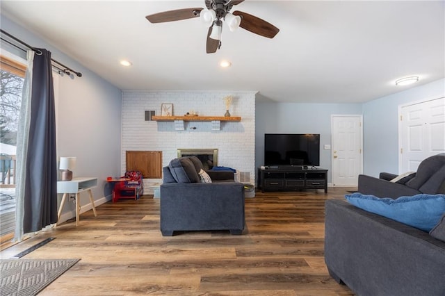 living room with ceiling fan, dark hardwood / wood-style flooring, and a brick fireplace