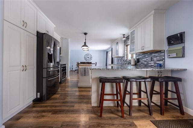 kitchen featuring tasteful backsplash, light stone countertops, white cabinets, black fridge, and kitchen peninsula